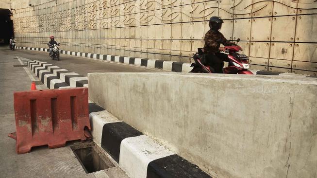 Kendaraan melintas di samping penutup saluran air atau "steel grating" yang hilang di jalur Lintas Bawah Mampang-Kuningan, Jakarta, Sabtu (25/8). [Suara.com/Muhaimin A Untung]