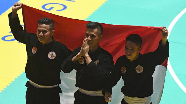 Tim silat Indonesia peraih medali emas Nunu Nugraha (tengah), Asep Yuldan Sani (kiri) dan Anggi Faisal Mubarok (kanan) merayakan kemenangan dengan membentangkan bendera merah putih usai meraih medali emas dalam final beregu putra pencak silat seni Asian Games 2018 di Padepokan Pencak Silat Taman Mini Indonesia Indah (TMII), Jakarta, Senin (27/8). ANTARA FOTO/INASGOC/Melvinas Priananda