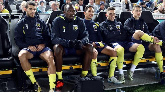 Mantan sprinter Usain Bolt tampak antusias di bangku cadangan, jelang diturunkan dalam pertandingan bola perdananya bersama klub Central Coast Mariners (CCM), melawan tim seleksi setempat di Gosford, New South Wales, Australia, Jumat (31/8/2018) malam. [Andrew Murray/AFP]