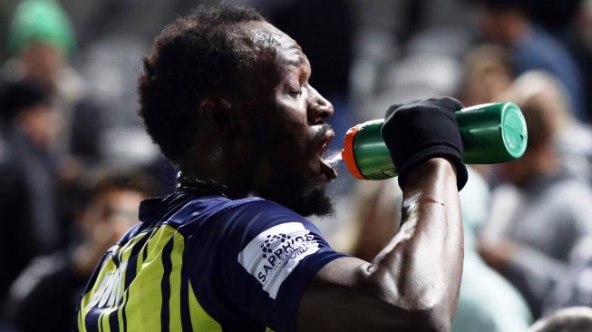 Mantan sprinter Usain Bolt meneguk air minum di sela-sela pertandingan bola perdananya bersama klub Central Coast Mariners (CCM), melawan tim seleksi setempat di Gosford, New South Wales, Australia, Jumat (31/8/2018) malam. [Andrew Murray/AFP]