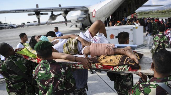 Warga yang terluka digotong personel TNI untuk dievakusi dengan pesawat Hercules di Bandara Mutiara Sis Al Jufri Palu, Sulawesi Tengah, Minggu (30/9). [ANTARA FOTO/Hafidz Mubarak]
