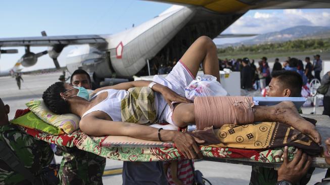 Warga yang terluka digotong personel TNI untuk dievakusi dengan pesawat Hercules di Bandara Mutiara Sis Al Jufri Palu, Sulawesi Tengah, Minggu (30/9). [ANTARA FOTO/Hafidz Mubarak]
