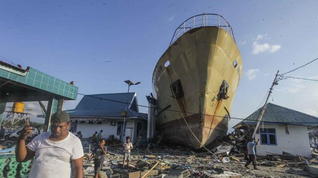 Warga melintas di depan kapal Sabuk Nusantara 39 yang terdampar ke daratan di desa Wani, Pantai Barat Donggala, Sulawesi Tengah, Senin (1/10). [ANTARA FOTO/Muhammad Adimaja]