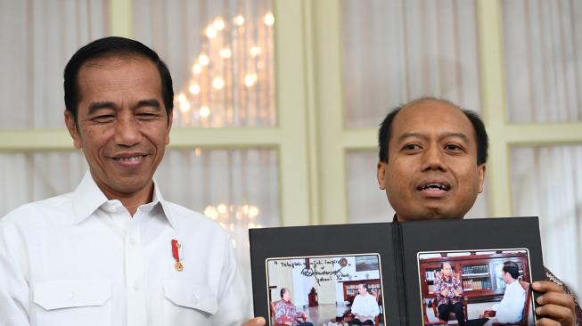 Presiden Joko Widodo (kiri) menyaksikan Kepala Pusat Data, Informasi, dan Humas Badan Nasional Penanggulangan Bencana (BNPB) Sutopo Purwo Nugroho memperlihatkan dokumentasi pertemuan mereka di Istana Bogor, Jawa Barat, Jumat (5/10). ANTARA FOTO/Wahyu Putro