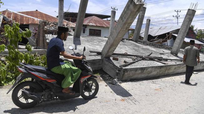 Umat islam melintas didekat bangunan yang roboh akibat gempa seusai melaksanakan Salat Jumat di Masjid An-Nur, Biromaru, Sigi, Sulawesi Tengah, Jumat (5/10).[ANTARA FOTO/Hafidz Mubarak]
