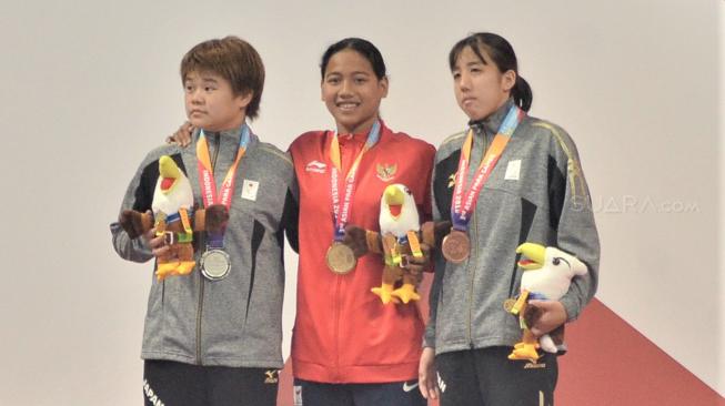 Ekspresi atlet para renang putri Indonesia Syuci Indriani (Tengah) usai meraih medali emas pada final renang nomor 100 meter putri gaya dada SB14 di Stadion Aquatic, Senayan, Jakarta, Senin (8/10). [Suara.com/Muhaimin A Untung]