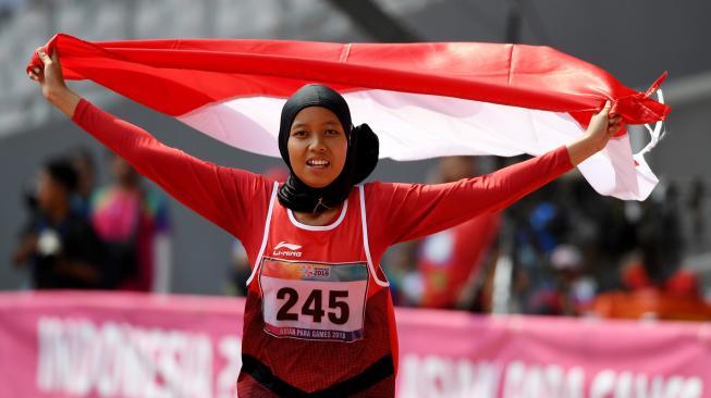 Sprinter Indonesia Karisma Evi Tiarani mengibarkan bendera merah putih usai finis terdepan dalam nomor 100 meter putri T42 dan T63 Asian Para Games 2018 di Stadion Utama Gelora Bung Karno, Jakarta, Rabu (10/10). [ANTARA FOTO/Akbar Nugroho Gumay]