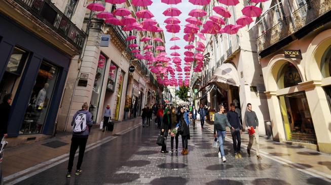 Pejalan kaki melintasi ratusan payung pink yang digantung di Montpellir, Prancis, Selasa (9/10). [AFP/PASCAL GUYOT]

