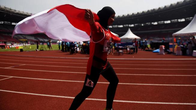 Sprinter Indonesia Karisma Evi Tiarani mengibarkan bendera merah putih usai finis terdepan dalam nomor 100 meter putri T42 dan T63 Asian Para Games 2018 di Stadion Utama Gelora Bung Karno, Jakarta, Rabu (10/10). [ANTARA FOTO/Akbar Nugroho Gumay]