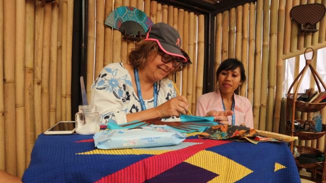 Seorang delegasi Annual Meeting IMF - WB 2018 dari luar negeri tertarik untuk belajar melukis kipas khas Bali di Indonesia Pavilion, Nusa Dua Bali. (Foto: Dok. Indonesia Pavilion)