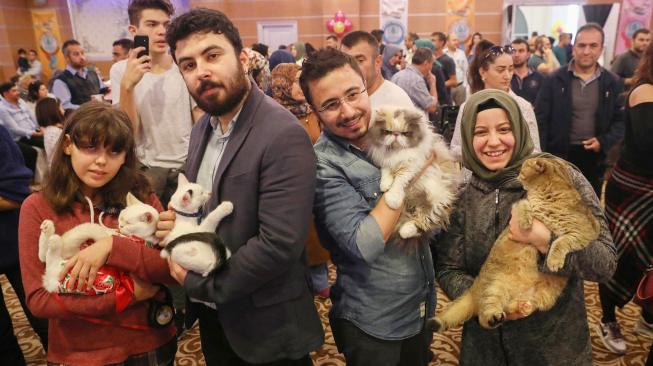 Orang-orang berpose dengan kucing mereka selama kontes kecantikan kucing internasional ke-3 di Ankara, Turki, Jumat (14/10). [AFP/ADEM ALTAN]