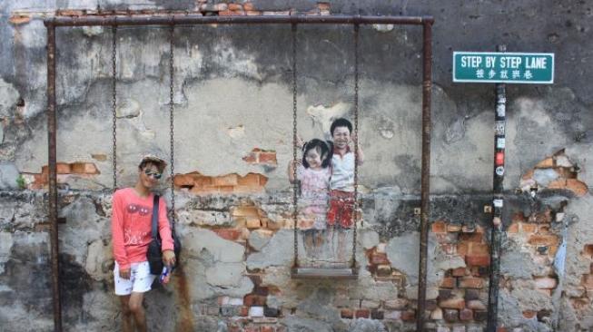 Pengunjung berpose di Penang Street Art Mural. (Suara.com/Silfa Humairah)