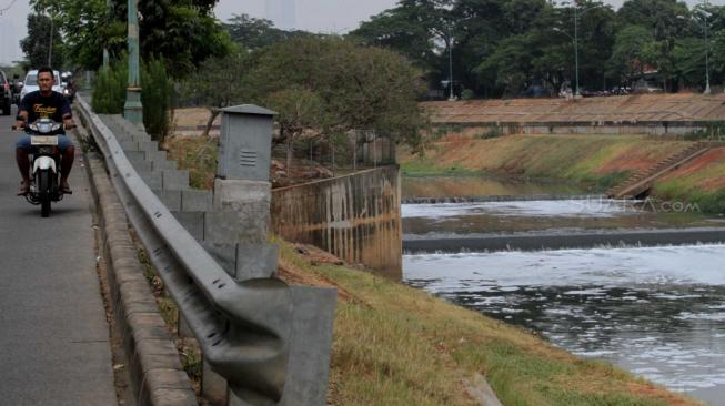 Pengendera motor melintas di samping  Kanal Banjir Timur (KBT) yang dipenuhi busa di Cipinang Besar Selatan, Jakarta Timur, Senin (22/10). (Suara.com/Fakhri Hermansyah)