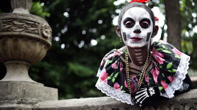 Seorang wanita menghias dirinya seperti seorang yang telah mati di perayaan Day of the Dead 2018 di kota Meksiko, Minggu (21/10). [Afp Photo/Rodrigo Arangua]