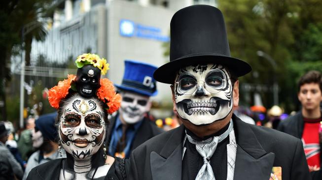 Seorang wanita dan Pria menghias dirinya seperti seorang yang telah mati di perayaan Day of the Dead 2018 di kota Meksiko, Minggu (21/10). [Afp Photo/Rodrigo Arangua]