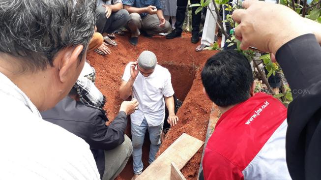 Putra sulung George Taka, Ahmad Zulfikar mengubur dan mengazani jenazah sang ayah. (Ismail/Suara.com)