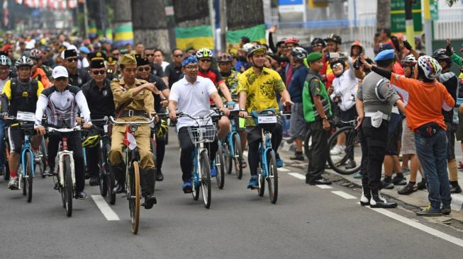 Presiden Joko Widodo mengenakan baju pejuang Bung Tomo didampingi Kepala Staf Presiden Moeldoko (kiri) dan Gubernur Jawa Barat Ridwan Kamil (ketiga kiri) menyapa warga ketika mengikuti kegiatan sepeda bersama dengan tema Bandung Lautan Sepeda di Bandung, Jawa Barat, Sabtu (10/11/2018). ANTARA FOTO/Wahyu Putro A