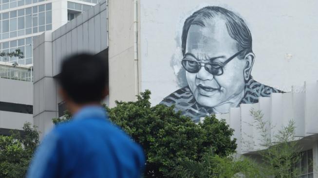 Seorang melintas di depan mural tokoh HB Jassin di Gedung Taman Ismail Marzuki, Jakarta, Senin (12/10). [Suara.com/Muhaimin A Untung] 