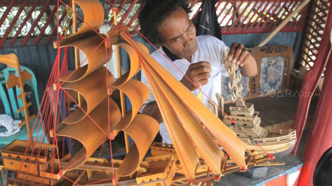 Pengrajin miniatur kapal pinisi menyelesaikan proses pembuatan di Marunda, Jakarta Utara, Selasa (13/11).(Suara.com/Fakhri Hermansyah)