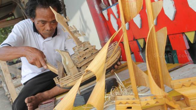 Pengrajin miniatur kapal pinisi menyelesaikan proses pembuatan di Marunda, Jakarta Utara, Selasa (13/11).(Suara.com/Fakhri Hermansyah)