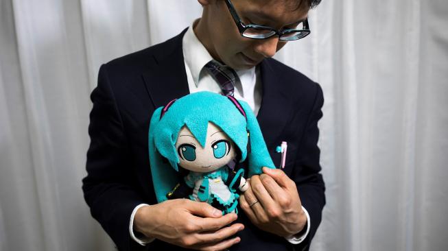 Akihiko Kondo berpose dengan bonek aktris virtual, Hatsume Miku sambil mengenakan cincin kawin di Tokyo, Jepang, Sabtu (10/11). (AFP/Behrouz MEHRI)