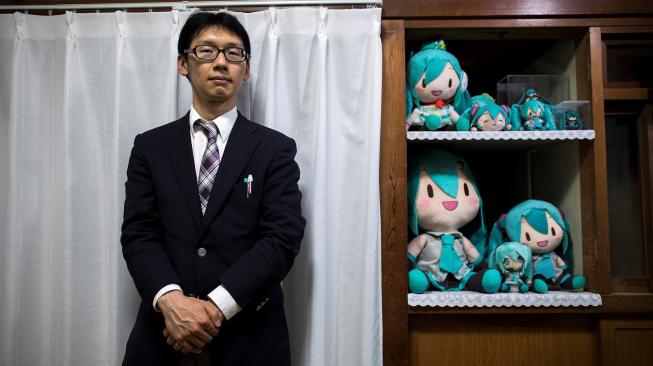 Akihiko Kondo berpose di sebelah boneka aktris virtual, Hatsune Miku di Tokyo, Jepang, Sabtu (10/11). (AFP/Behrouz MEHRI)