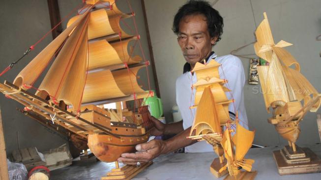 Pengrajin miniatur kapal pinisi menyelesaikan proses pembuatan di Marunda, Jakarta Utara, Selasa (13/11).(Suara.com/Fakhri Hermansyah)