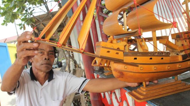 Pengrajin miniatur kapal pinisi menyelesaikan proses pembuatan di Marunda, Jakarta Utara, Selasa (13/11).(Suara.com/Fakhri Hermansyah)