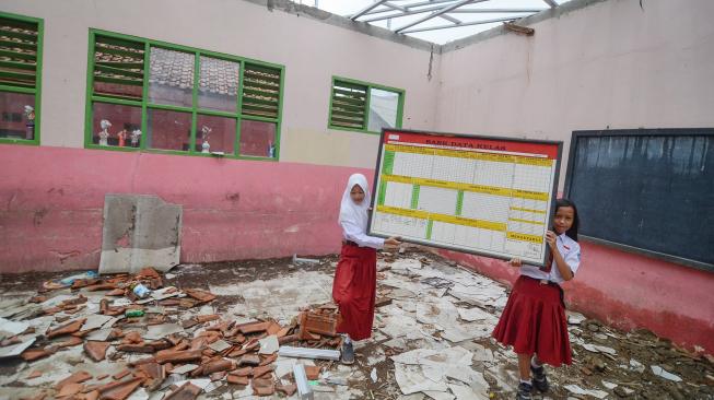 Siswa memindahkan papan bank data kelas yang atapnya ambruk di SDN Tegallaja, Desa Sukatani, Kabupaten Bandung Barat, Jawa Barat, Rabu (14/11). [ANTARA FOTO/Raisan Al Farisi]