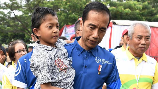 Presiden Joko Widodo (kiri) menggendong siswa penyandang disabilitas asal Sukabumi Mukhlis Abdul Holik disela Peringatan Hari Disabilitas Internasional Tahun 2018 di Bekasi, Jawa Barat, Senin (3/12). [ANTARA FOTO/Puspa Perwitasari]