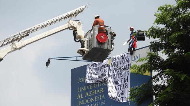 Seorang pria memanjat baliho di kawasan Kampus Universitas Al Azhar Jalan Sisingamangaraja, kebayoran Baru, Jakarta Selatan, Kamis (6/12). [Suara.com/Muhaimin A Untung]