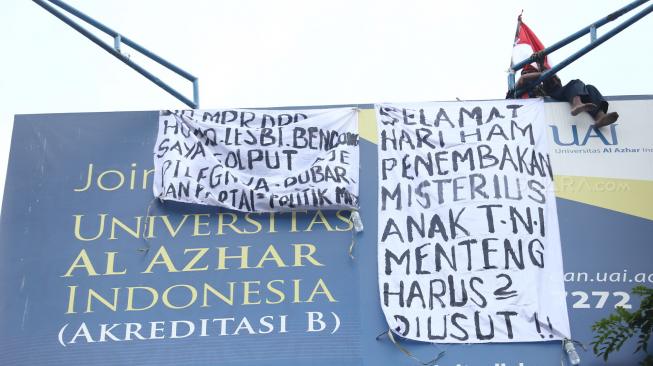 Seorang pria memanjat baliho di kawasan Kampus Universitas Al Azhar Jalan Sisingamangaraja, kebayoran Baru, Jakarta Selatan, Kamis (6/12). [Suara.com/Muhaimin A Untung]