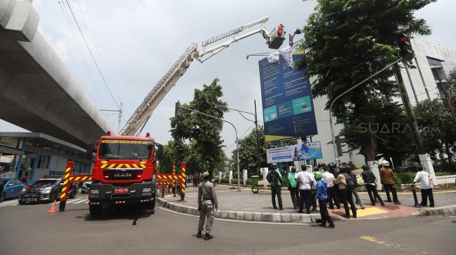 Seorang pria memanjat baliho di kawasan Kampus Universitas Al Azhar Jalan Sisingamangaraja, kebayoran Baru, Jakarta Selatan, Kamis (6/12). [Suara.com/Muhaimin A Untung]