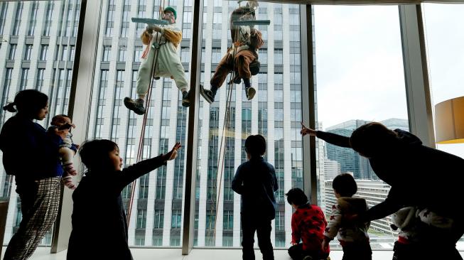 Petugas pembersih jendela berpakaian seperti anjing dan babi hutan membersihkan jendela-jendela hotel Ryumeikan, di Tokyo, Jepang, Kamis (13/12). [Kazuhiro NOGI / AFP]