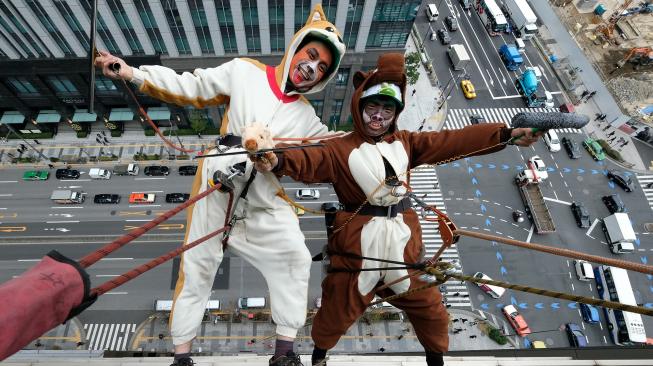 Petugas pembersih jendela berpakaian seperti anjing dan babi hutan membersihkan jendela-jendela hotel Ryumeikan, di Tokyo, Jepang, Kamis (13/12). [Kazuhiro NOGI / AFP]