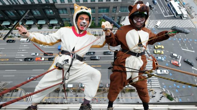 Petugas pembersih jendela berpakaian seperti anjing dan babi hutan membersihkan jendela-jendela hotel Ryumeikan, di Tokyo, Jepang, Kamis (13/12). [Kazuhiro NOGI / AFP]