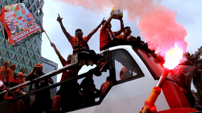 Pendukung Persija Jakarta The Jak mania menyambut iring-iringan pemain beserta  official di Thamrin, Jakarta Pusat, Sabtu (15/12).  [Suara.com/Fakhri Hermansyah]