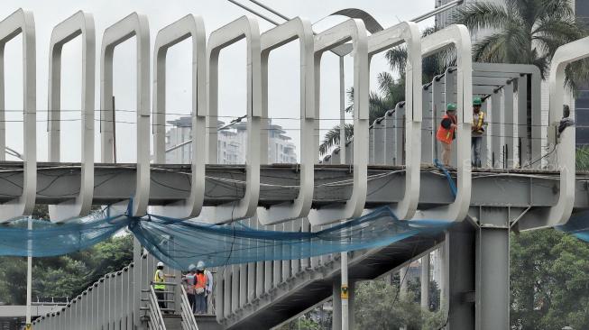 Pekerja melakukan pengerjaan proyek revitalisasi Jembatan Penyeberangan Orang (JPO) Bundaran Senayan di Jakarta, Selasa (18/12). [Suara.com/Muhaimin A Untung]