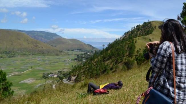 Wisatawan tampak berfoto di sekitar bukit dan persawahan kaki gunung Pusuk Buhit. (Suara.com/Silfa Humairah)