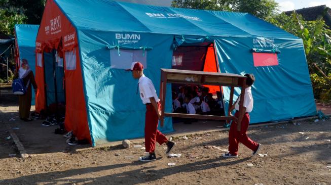 Sejumlah siswa SD Yayasan Madrasah Ibtidaiyah (MI) Darussalam Sukaraja mengangkat meja dan kursi dari sekolah mereka menuju tenda darurat untuk kegiatan belajar mengajar di Desa Sukaraja, Kabupaten Lampung Selatan, Lampung, Senin (7/1). ANTARA FOTO/Ardiansyah