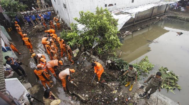 Petugas PPSU membersihkan lumpur yang menggenangi jalan pemukiman warga karena tanggul aliran Kali Pulo jebol di Kelurahan Jati Padang, Kecamatan Pasar Minggu, Jakarta, Senin (14/1). [ANTARA FOTO/Muhammad Adimaja]