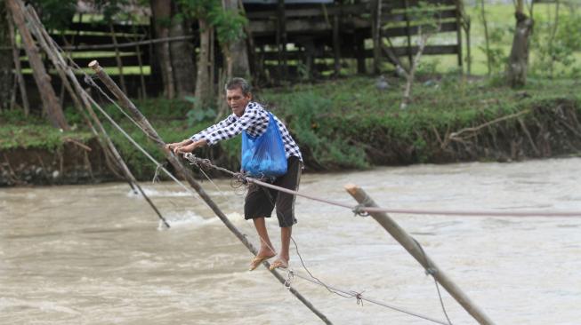 Warga menyeberangi sungai Krueng Meureubo dengan menggunakan jembatan tali yang terbuat dari kabel listrik menuju Desa Sikundo, Kecamatan Pante Ceureumen, Aceh Barat, Aceh, Sabtu (2/1). ANTARA FOTO/Syifa Yulinnas