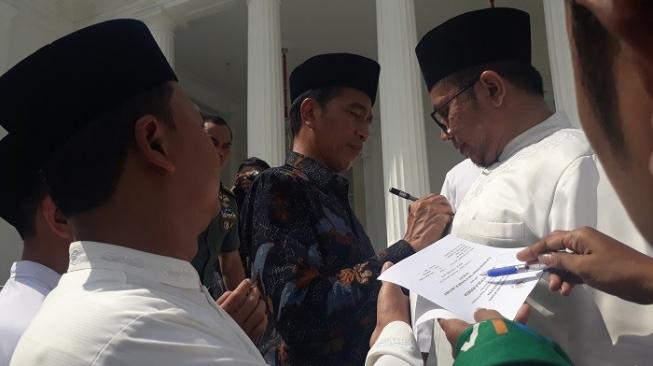 Presiden Jokowi membubuhkan tanda tangan di baju koko ulama. (Suara.com/Ummi H.S)