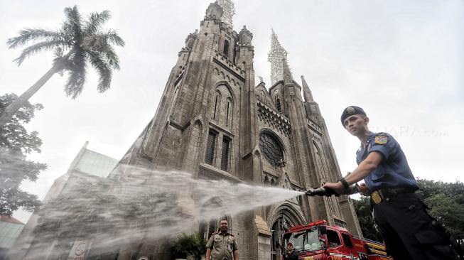 Sejumlah petugas Damkar membersihkan Gereja Katedral dan Masjid Istiqlal di Jakarta, Selasa (12/2). [Suara.com/Muhaimin A Untung]