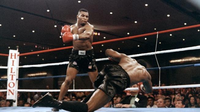 Mike Tyson (kiri) memukul KO penantangnya, Trevor Berbick, yang sekaligus membuatnya mencatat sejarah sebagai petinju termuda yang menjadi juara dunia kelas berat, dalam duel di Las Vegas, AS, 22 November 1986. [AFP/Carlos Schiebeck]