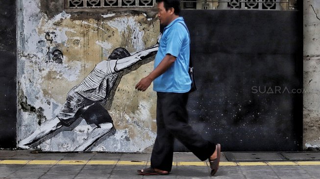 Warga melintas di depan mural kawasan Berok, Penjaringan, Jakarta Utara, Minggu (24/2). [Suara.com/Muhaimin A Untung]