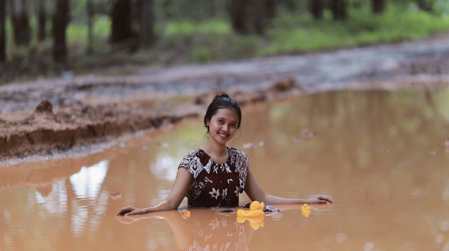 Seorang gadis berkubang lumpur di jalanan rusak di Batumarta, OKU, Sumatera Selatan. Foto ini adalah bentuk kritik atas jalanan rusak di kawasan tersebut. [Facebook/Robby Ari Sanjaya]
