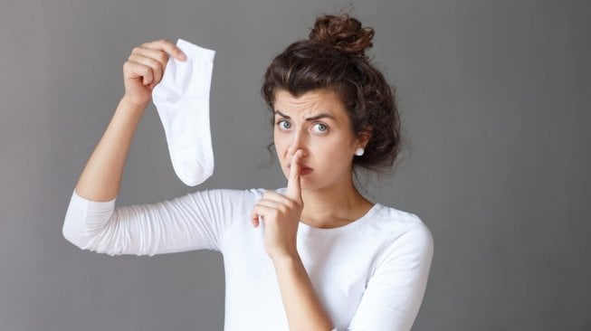 Perempuan memegang kaos kaki bau. (Shutterstock)