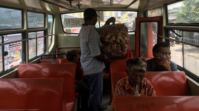 Pedagang asongan tengah menjajakan dagangan di dalam Metro Mini yang sepi penumpang, Terminal Senen, Kamis (28/2/2019). [Suara.com/Erick Tanjung]