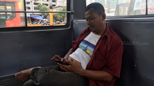 Sopir metromini tampak bersantai di dalam busnya karena sepi penumpang, Kamis (28/2/2019). [Suara.com/Erick Tanjung]